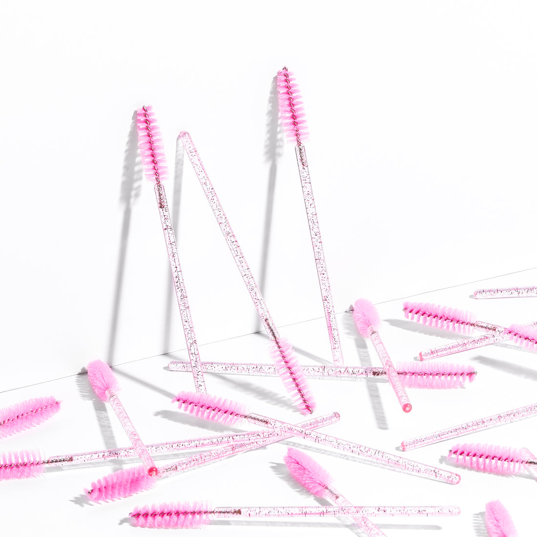 Disposable eyelash brushes are scattered against a white background