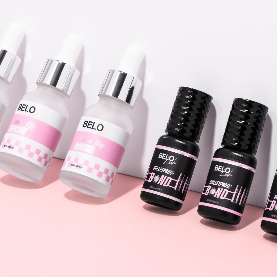 A line of lash adhesive bottles lean against a wall