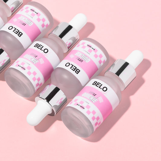 Bottles of lash adhesive are lined up on a pink background