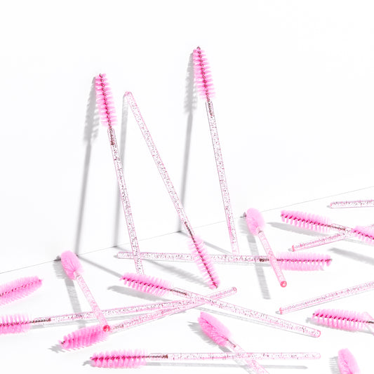 Disposable eyelash brushes are scattered against a white background