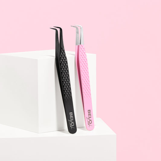 Two pairs of lash tweezers leant against a white block, against a pink background.