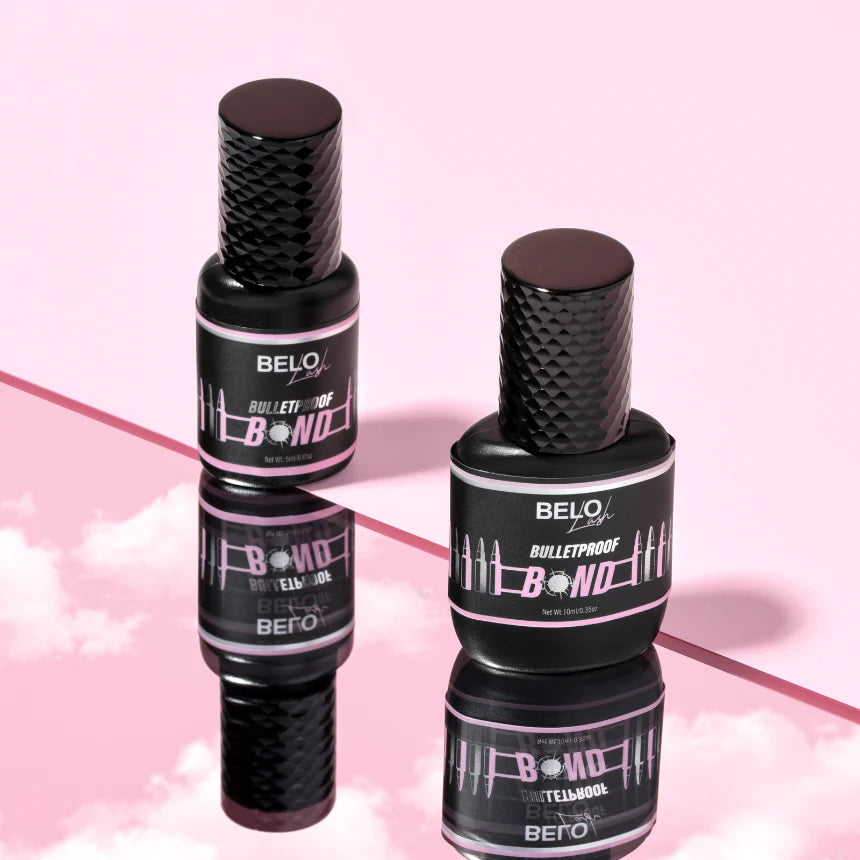 Two bottles of lash glue stood on a sky surface and against a pink background.